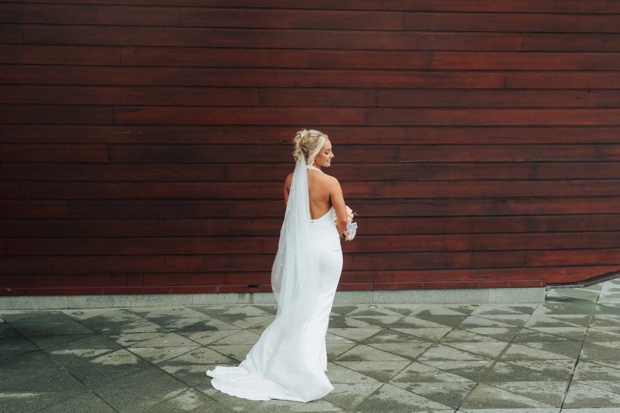 The bride in her gown, holding her bouquet against a warm timber wall