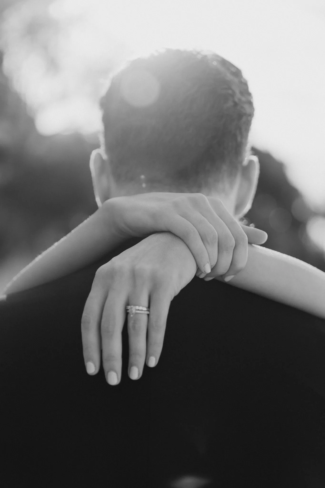 The groom holds the bride from behind in a quiet moment, in black and white